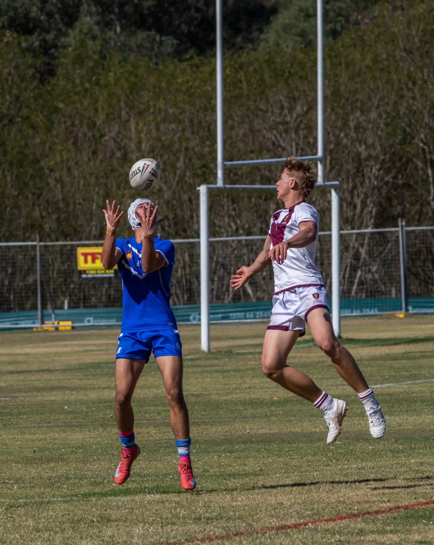 Two rugby players contesting a high ball on a grass field